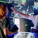 Controllers interact with advanced airspace surveillance and automation displays at a Collins Aerospace facility, supported by radar systems